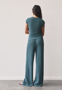 Teal ribbat loungedräkt med kortärmad topp och vida byxor, tillverkad av mjukt, texturerat tyg med en avslappnad passform.