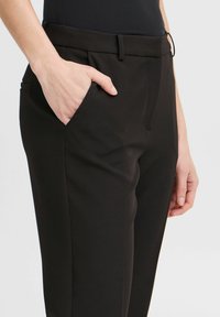 Čierne nohavice s prispôsobeným strihom, hladkým dizajnom, prednými vreckami a jemnou textúrou, zobrazené na neutrálnom pozadí.