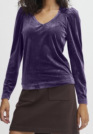 Haut en velours violet à manches longues avec un col en V et un détail froncé aux épaules, associé à une jupe marron dotée de deux poches avant.