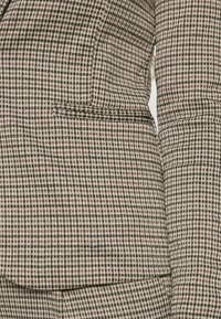 Brun och beige rutigt kavaj med en mjuk textur, med en enda bröstficka och strukturerade slag.