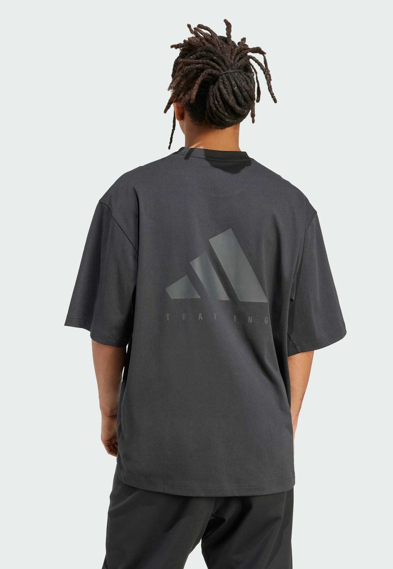 Musta ylisuuri puuvillainen treenipaita lyhyillä hihoilla, jossa on suuri harmaa Adidas-logo ja "TRAINING"-teksti selkäpuolella.