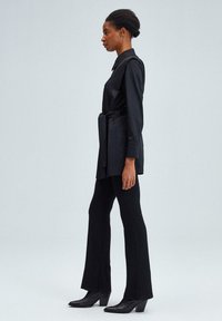 Abito camicia nero con cintura, dotato di colletto, abbinato a pantaloni neri a palazzo aderenti e stivali con tacco a blocco. Tessuto liscio e design su misura.