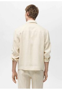Ljusbeige linneskjorta med uppvikta ärmar, ryggsöm och en avslappnad passform. Minimalistisk design utan synlig hårdvara eller mönster.