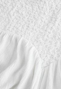 Tissu blanc texturé arborant un motif en relief et gonflé, accompagné d'un matériau lisse et froissé, créant un effet visuel et tactile contrasté.