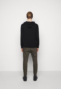 Felpa nera con vestibilità rilassata, maniche lunghe e tasca a marsupio. Abbinata a pantaloni verdi oliva a gamba affusolata e scarpe nere.