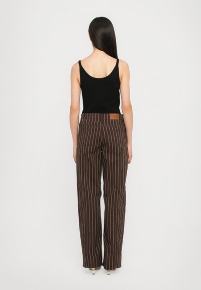 Brown striped wide-leg pants with a high waist, detailed stitching, and a leather patch on the back waistband. Paired with a black tank top.