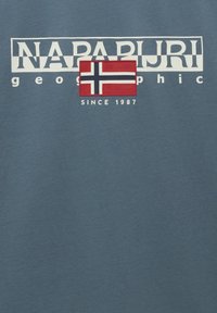 T-shirt in cotone blu con logo "NAPAPIJRI" in bianco, patch della bandiera norvegese rossa e il testo "SINCE 1987" sotto la bandiera.