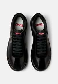 Sneaker nere con tomaia in pelle texturizzata, caratterizzate da lacci neri, un logo rosso "CAMPER" sulla linguetta e una sezione di contrasto sulla punta.