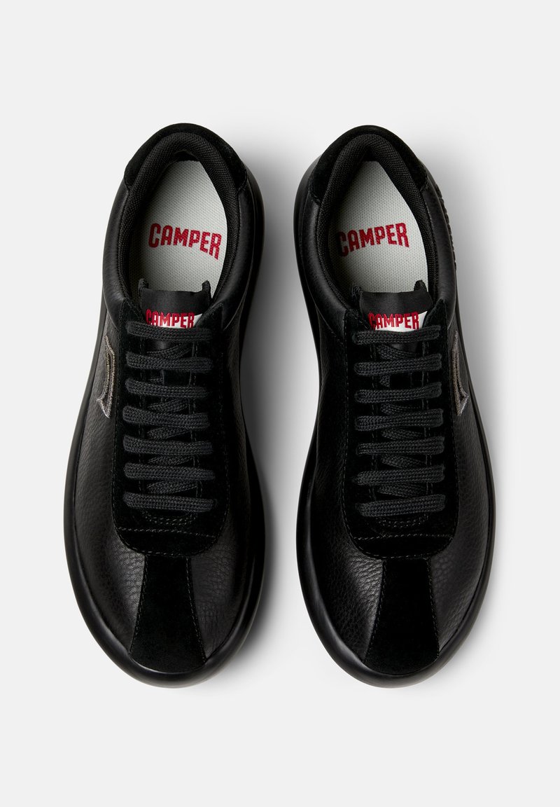 Zwarte sneakers met een leren bovenwerk met textuur, voorzien van zwarte veters, een rood "CAMPER" logo op de tong en een contrasterend deel op de neus.