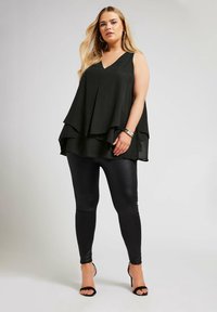 Svart lagerpå, utan ärmar, med V-hals, bärs med glansiga svarta leggings och öppna klackar. Slät tyg med mjuka draperingsdetaljer.