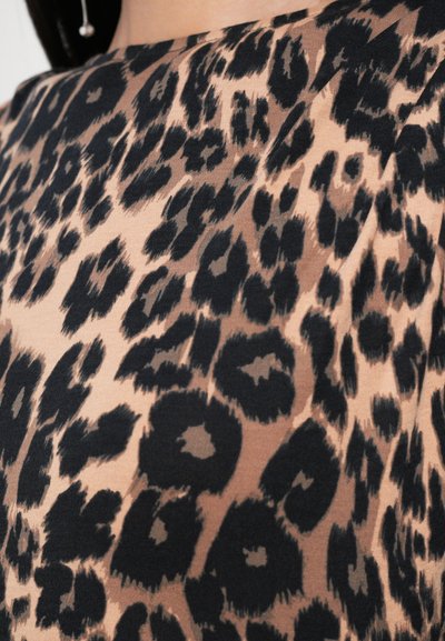 Uski blizu crno-smeđe tkanine s leopard uzorkom nosi osoba s vidljivom crnom kosom i visećom bisernom naušnicom.