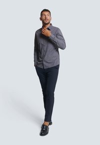 Langemouwen knoopshirt met een marineblauw en wit geometrisch patroon, gecombineerd met slim-fit marineblauwe broek en zwarte loafers.