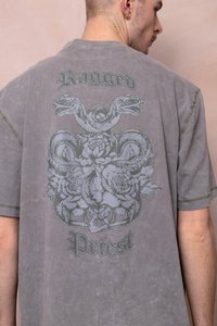 Grijze oversized t-shirt met een centrale grafiek van verstrengelde slangen en bloemen, met de tekst "Ragged" en "Priest" in gestileerd lettertype.