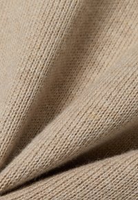 Nahaufnahme eines beigen Strickstoffs mit feiner, weicher Textur, sichtbaren Maschen und sanften Falten.