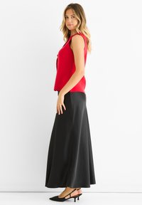 Red sleeveless top with a slight drape, paired with a long black satin skirt. Black pointed-toe heels complete the outfit.