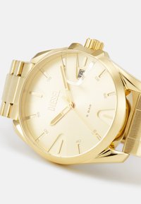 Goldfarbene Edelstahl-Uhr mit rundem Ziffernblatt, minimalistischen Stundenmarkierungen, Datumsanzeige und gebürsteter Oberfläche am Armband.