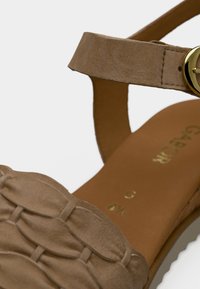 Μπεζ σατέν σανδάλι με πλεκτό σχέδιο πάνω από τα δάχτυλα και λείο λουράκι στον αστράγαλο. Διαθέτει στρογγυλό αγκράφα σε χρυσό τόνο και καφέ πάτο.