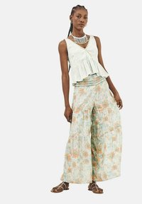 Blusa peplum verde claro con manchas blancas, combinada con pantalones de pierna amplia con flores en suaves tonalidades de azul, naranja y blanco. Sandalias con tiras completan el look.