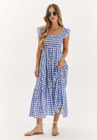 Modrá a biela károvaná šaty s vrstvenou sukňou, pufovanými rukávmi a kvetinovými akcentmi. Vyrobené z ľahkého materiálu. Má štvorcový výstrih.