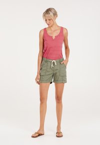 Roze mouwloos topje met een keyhole-halslijn, gecombineerd met groene shorts met een elastische tailleband en voorzakken.