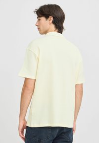 Kortermet polo skjorte i lys gul, lagd av teksturert vaffelstoff. Har klassisk krage og avslappet passform, stylet med minimal detaljer.