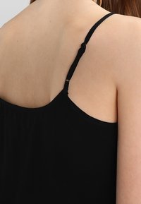 Svart linne med justerbara tunna axelband, veckad tyg bak och en slät yta. Enkelt design med minimal detaljering.