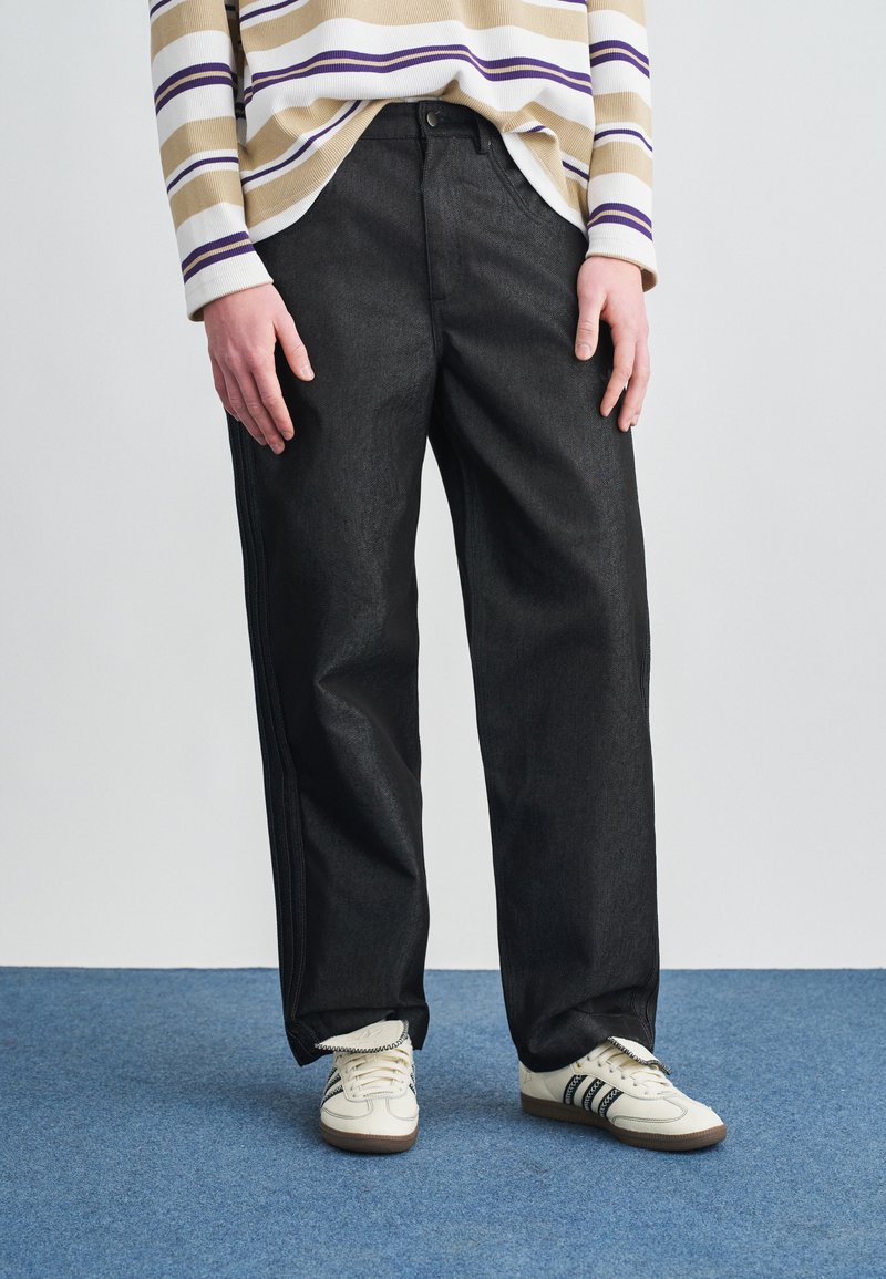 Crne, široke traperice izrađene od trapera, s čistim dizajnom i blago sjajnom teksturom, u kombinaciji s bijelim tenisicama s crnim prugama.