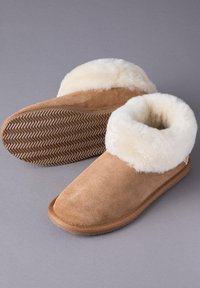 Tan suede slippers with a soft white fur cuff, flat rubber sole featuring a herringbone pattern, rounded toe, and no visible branding.