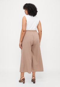Lightweight, loose-fit beige culottes with an elastic waistband, paired with a sleeveless white top and leopard print block-heeled sandals.