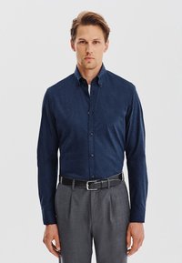 Granatowa koszula z guzikami, wykonana z teksturowanej tkaniny, z klasycznym kołnierzykiem, prostymi guzikami z przodu i długimi rękawami, w zestawie z szarymi spodniami.