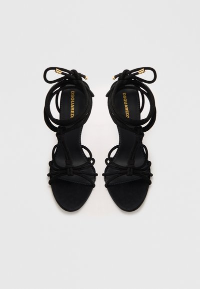 Svarta mocka högklackade sandaletter med dekorativa knutna remmar och guldaccenter. Slät innerfoder med en texturerad fotbädd.