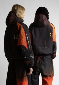 Melni un oranži āra apģērba uzvalki ar kapucēm, kas izceļas ar lieliem grafiskajiem rakstiem, teksturētu audumu un elastīgām piedurknēm. Iekļautas arī atbilstošas bikses.