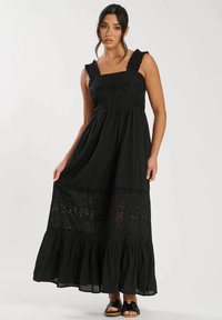 Svart maxiklänning med volangremmar, intrikata broderade detaljer och en flerfaldig kjol med utskurna mönster i nederkanten.