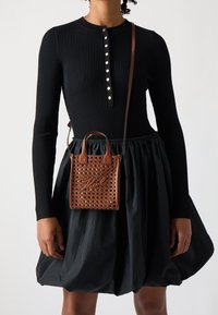 Czarny prążkowany top z długim rękawem i zapięciem na guziki, zestawiony z czarną, obszerną spódnicą. Brązowa pleciona torebka z podwójnymi uchwytami i charakterystycznym detalem.
