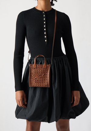 Czarny prążkowany top z długim rękawem i zapięciem na guziki, zestawiony z czarną, obszerną spódnicą. Brązowa pleciona torebka z podwójnymi uchwytami i charakterystycznym detalem.
