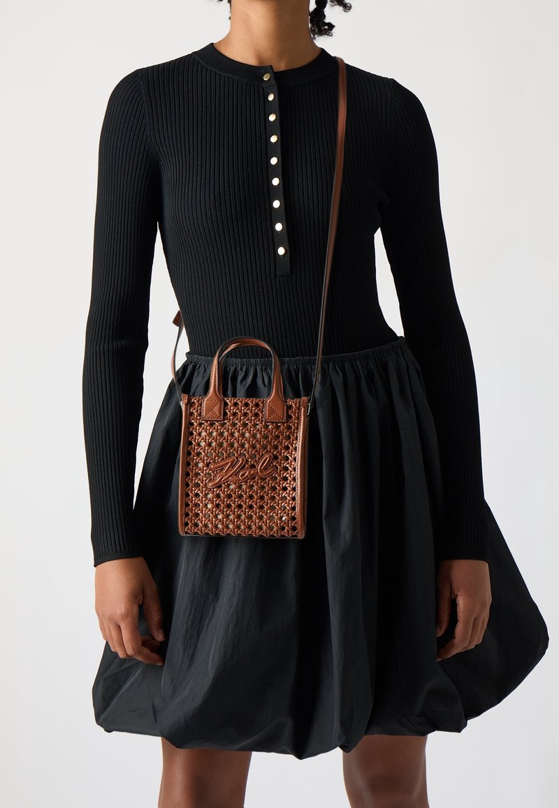 Czarny prążkowany top z długim rękawem i zapięciem na guziki, zestawiony z czarną, obszerną spódnicą. Brązowa pleciona torebka z podwójnymi uchwytami i charakterystycznym detalem.