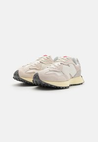 Beige Sneaker aus einer Mischung von Wildleder und Mesh-Materialien, mit einer gepolsterten Sohle, einem schwarzen Profilmuster und roten Akzenten auf der Zunge.