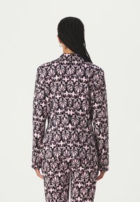 Patterned blazer in pink and black with leaf motifs, structured shape, long sleeves, and notched collar, worn with matching pants.