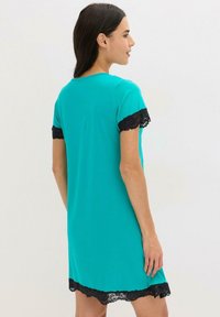 Abito corto turchese con pizzo nero ai bordi delle maniche e dell'orlo. Tessuto morbido; vestibilità casual e rilassata. Punto di contatto visibile sul retro.