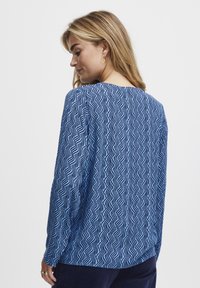 Blue long-sleeved top featuring a wave pattern in darker blue. Soft, textured fabric with a round neckline and relaxed fit.