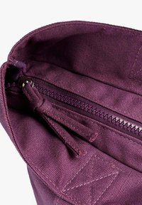 Interior de bolsa de tela púrpura con un cierre de cremallera suave, forro texturizado y detalles de costura decorativa a lo largo de los bordes.