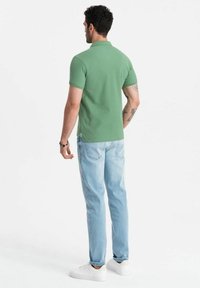 Polo vert à manches courtes, associé à un jean bleu clair et des baskets blanches. Texture subtile ; design simple et classique.