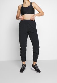 Svart sportbh och joggersbyxor med elastisk midja, ribbade detaljer och avsmalnande muddar, tillsammans med svarta sneakers.