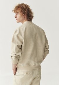 Beige bomberjakke med en tekstureret stof, ribbet manchetter og en afslappet pasform. Sættes sammen med matchende lyse bukser.