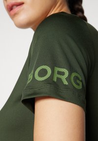 Sötétzöld, rövid ujjú ing sima textúrával, nagy zöld "ORG" felirattal a ujján, pöttyös betűtípussal.