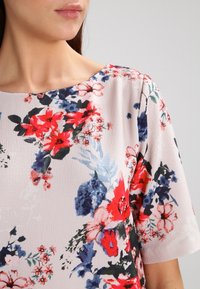 Květinová blůza s světle růžovým pozadím a červenými, modrými a zelenými květy; krátké rukávy a kulatý výstřih. Měkká textura.