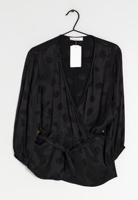 Zwarte wikkelblouse van gladde stof, met lange mouwen met elastische manchetten en een subtiel ton-sur-ton bloemenpatroon. Inclusief een strikdetail in de taille.