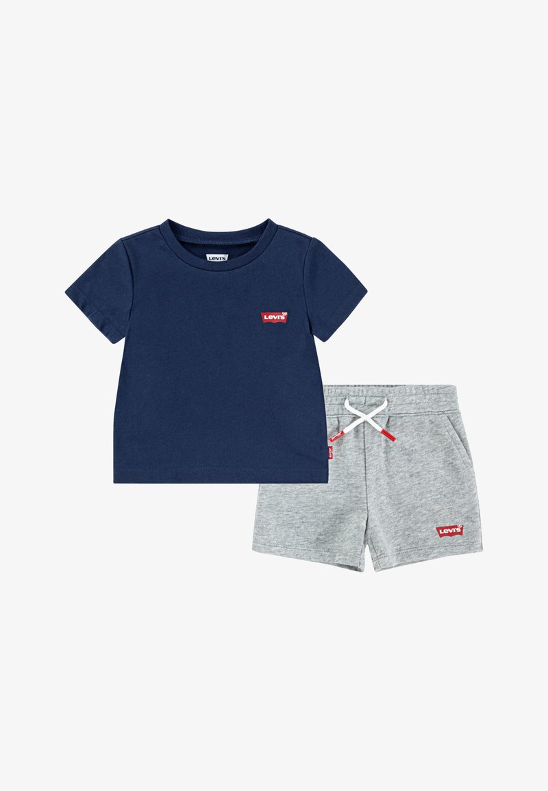 Jūras zila kokvilnas T-kreklu ar sarkano Levi's logo, kombinēts ar pelēkiem kokvilnas šortiem, kuriem ir aukliņa un mazs logotips uz apakšmala.