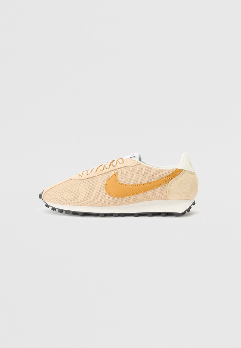 Beige och tan låg sko med övre i mesh och mocka, tan Nike swoosh-logga, vit sula och svart texturerad yttersula, visad i profil.