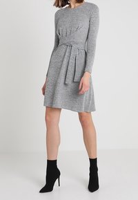 Grå långärmad klänning med figursydd bodice, veckdetalj framtill och knytet i midjan. Matchas med svarta ankelboots.